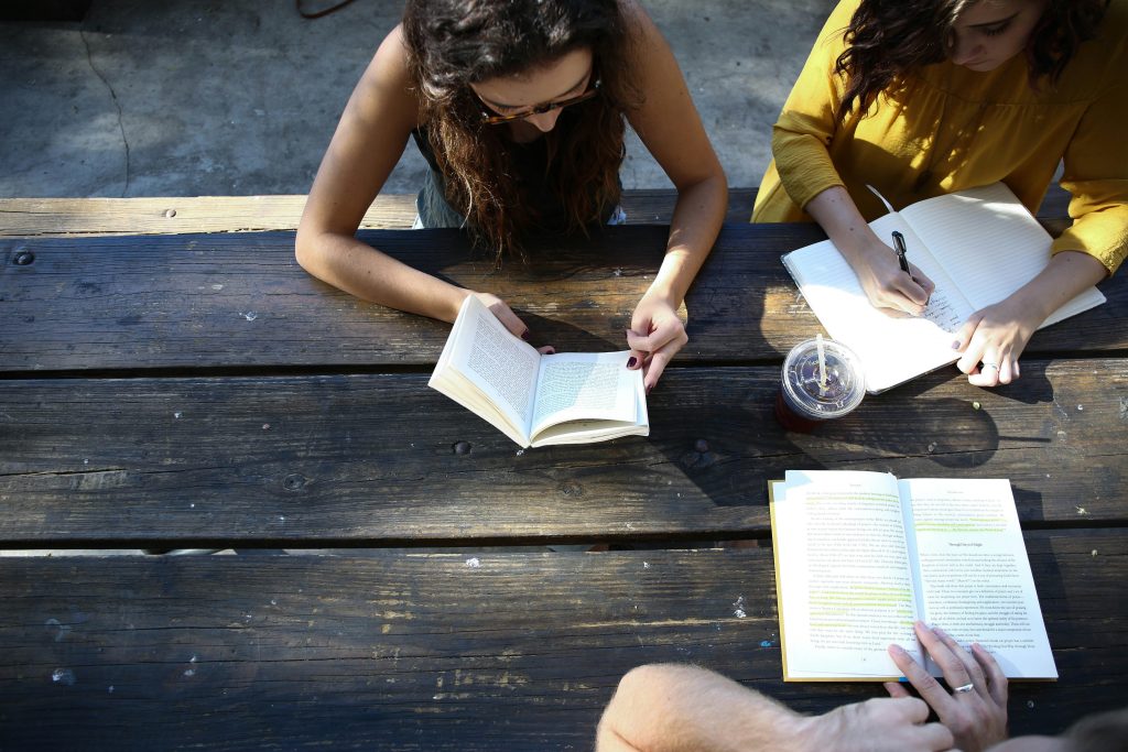 Three women reading outside at a picnic bench.